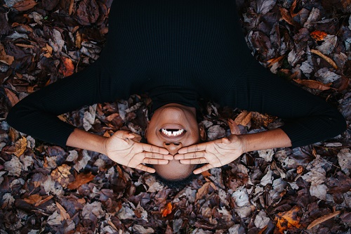 Femme allongée sur des feuilles d'automne souriant en se cachant les yeux avec les mains