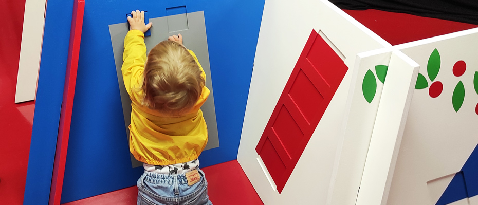 Un jeune enfant manipule des pièces en bois devant des panneaux également en boisà son niveau 