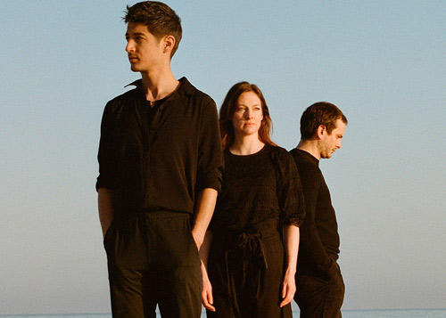 Les musiciens, 2 hommes, 1 femme, habillés de noir. Fond : ciel et mer