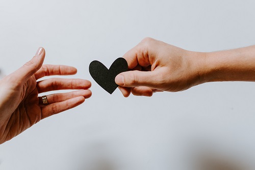 deux mains s'échangent un coeur en papier noir