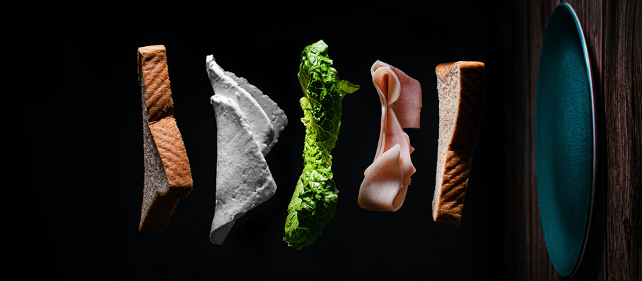 une tranche de pain, du jambon, du fromage, de la salade et une assiette en "lévitation" sur fond noir