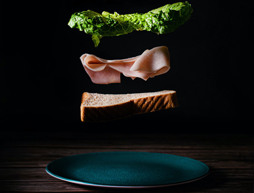 une tranche de pain, du jambon, de la salade et une assiette en "lévitation" sur fond noir