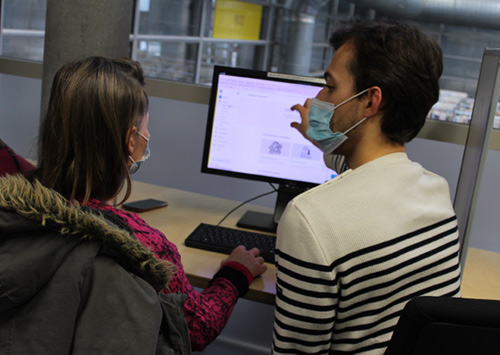 Le conseiller numérique en train d'accompagner un usager devant un ordinateur de la médiathèque.