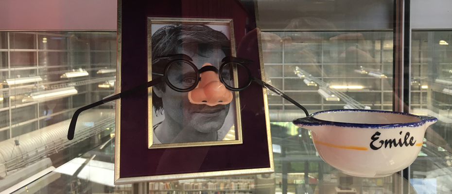 Vitrine contenant un cadre avec le portrait de Ronan Badel en noir et blanc + un faux nez et des lunettes rondes noires et un bol à oreilles avec l'annotation Emile dessus.