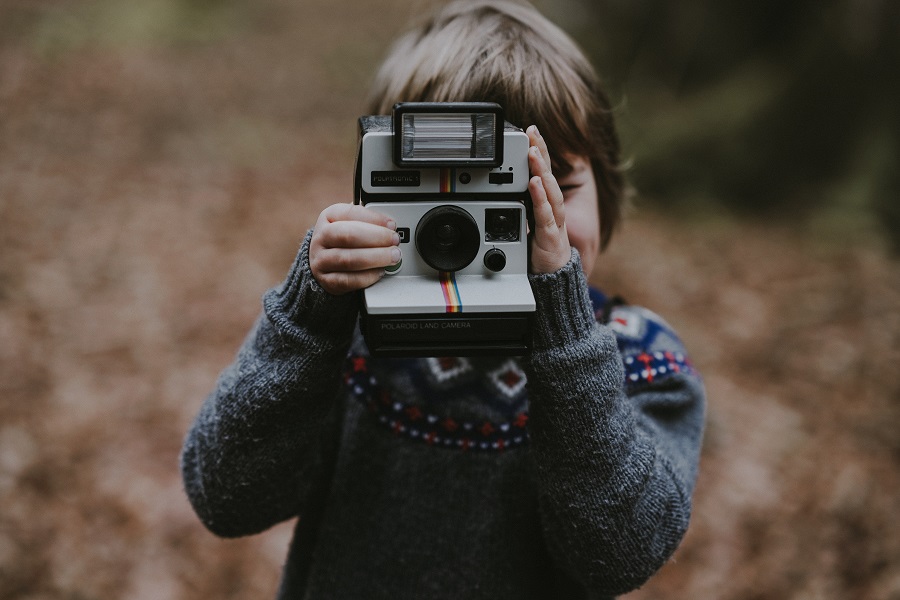 enfant de face tenant un polaroid devant son visage dans un paysage d'automne