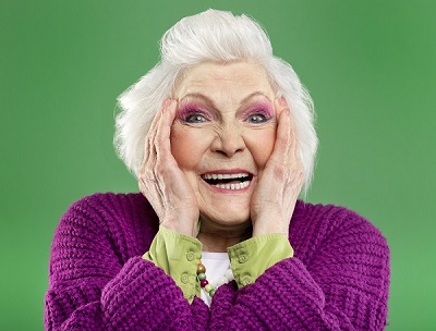 femme senior aux cheveux blancs portant un pull violet grimace de manière amusante