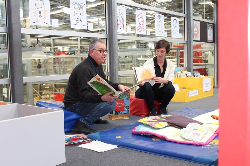Deux bibliothécaires assis, avec chacun un album ouvert sur leurs genoux