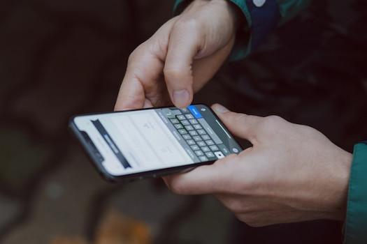 Mains tenant un téléphone mobile dont l'écran affiche un clavier