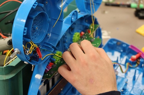 Une main tenant des fils électriques à l'intérieur d'un jouet en plastique bleu
