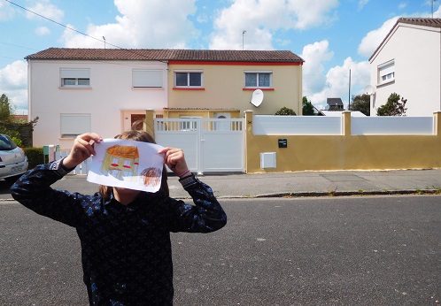 Enfant montrant un dessin devant une maison 