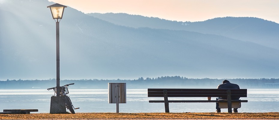personne seule assise sur un banc devant un plan d'eau face à une montagne 