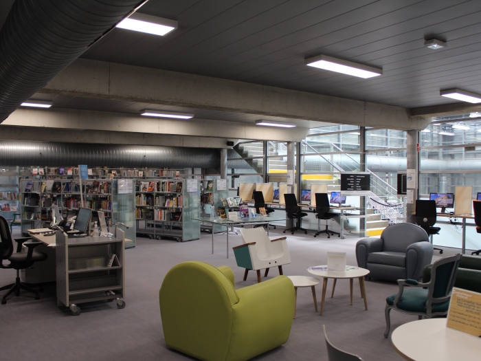 L'espace Atelier avec salon (premier plan), ordinateurs et étagères de livres