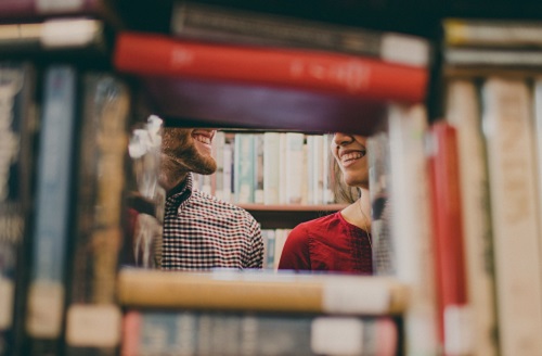 1 femme et 1 homme sourient à travers un rayonnage de livres 